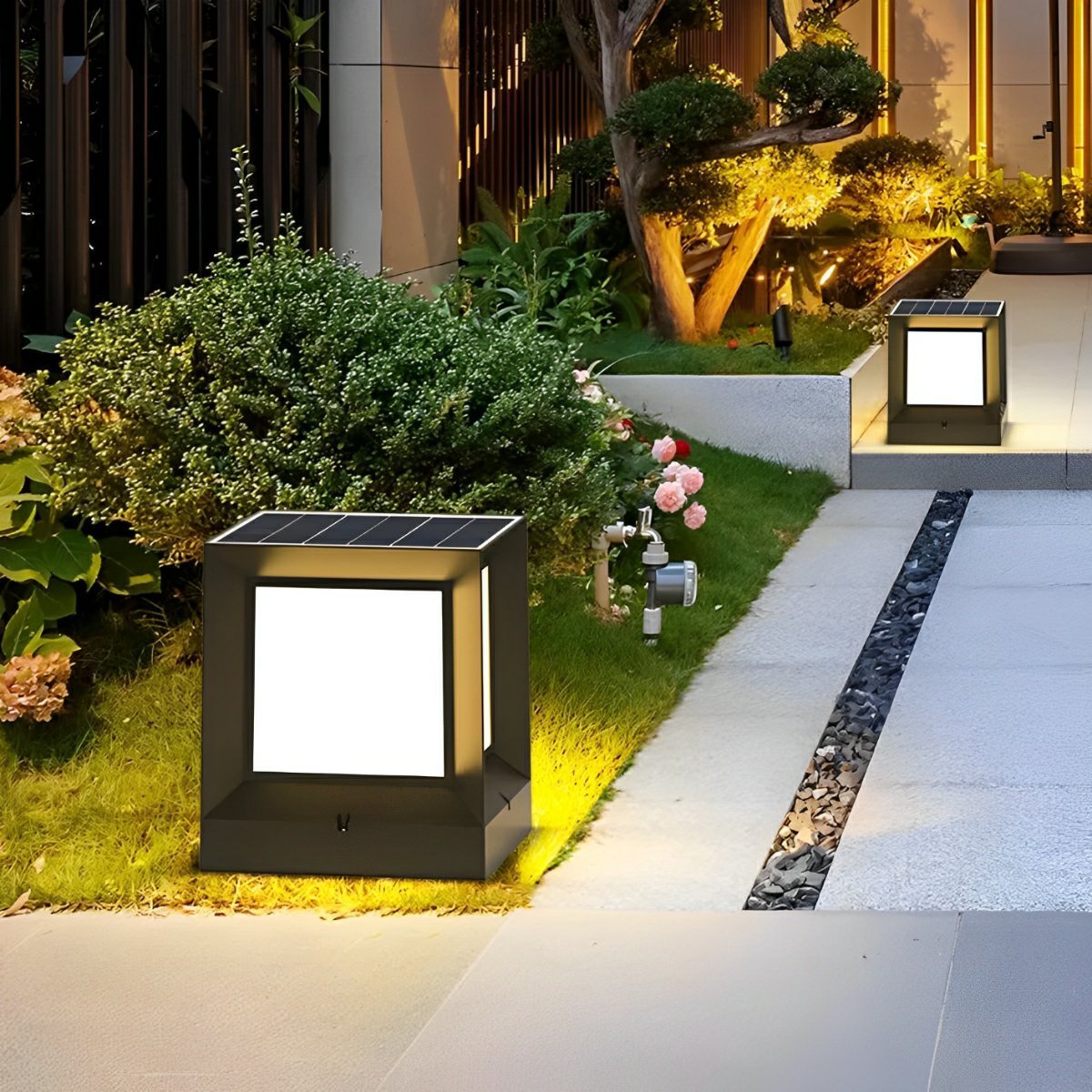 Square black solar post light with a glowing white panel on a lawn beside a garden path, second light on the steps behind